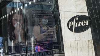 Ad for COVID-19 testing reflects on glass at a bus stop, as pedestrians walk past Pfizer world headquarters.