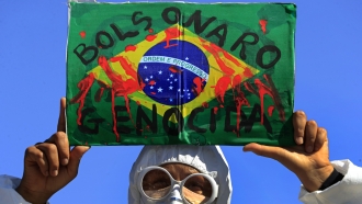 A demonstrator holds an image of the Brazilian flag covered in fake blood and the Portuguese phrase "Bolsonaro Genocide"