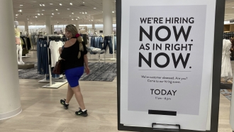 A customer walks behind a sign at a Nordstrom store seeking employees.