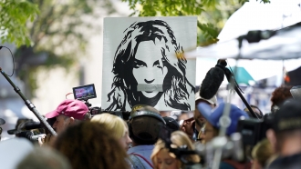 #FreeBritney protesters outside of a Los Angeles court house wave a poster of Britney Spears with her mouth covered.