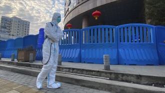 A worker in protective overalls and carrying disinfecting equipment walks outside the Wuhan Central Hospital
