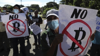 Demonstrators hold signs protesting El Salvador's adoption of Bitcoin as a legal national tender.
