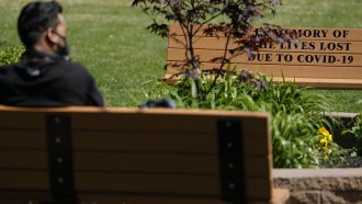 A man sits near a bench memorializing people who died from COVID-19