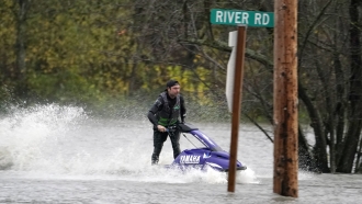 A man operates a personal watercraft along a road flooded by water from the Skagit River.