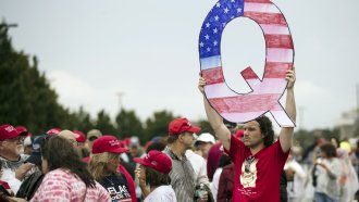 A man holds a poster of a Q with an American flag painted on it.
