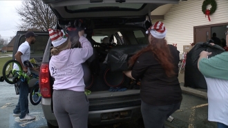 Women load bags of presents into the back of a car.