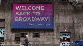 People walk a electronic board reading "Welcome Back to Broadway!" after cancellations of the broadway shows due to COVID-19