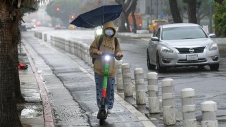 A woman with an umbrella rides her electric scooter through downtown Los Angeles.