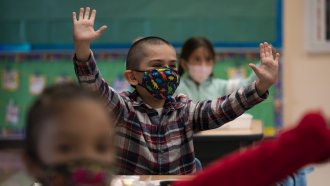 A masked student raises his hand in class.