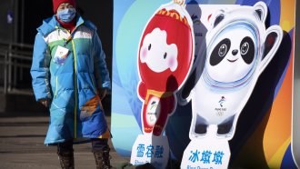 A woman in a face covering stands next to figures of the Winter Paralympic mascot in Beijing