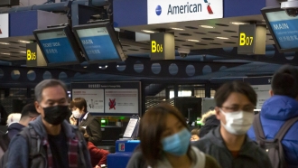 Travelers wearing face masks line up to check in for a flight.