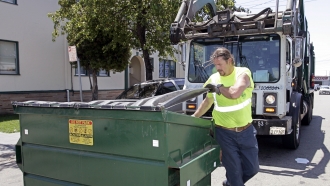 A garbage collector from Waste Management picks up garbage at an apartment complex