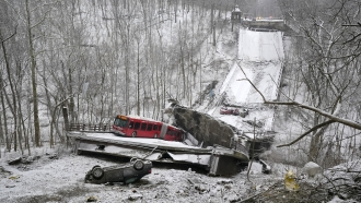 A collapsed bridge covered in snow with a bus and an overturned car.