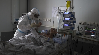 A medical staff member tends to a patient with COVID-19 at an ICU .