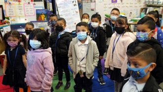 Kindergarteners wear masks while listening to their teacher