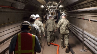 Members of the Navy and civilian water quality recovery experts walk through tunnels at the storage facility