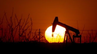 A pump jack operates as the Sun begins to set on the western horizon.