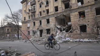 A man rides a bicycle in front of an apartment building damaged by shelling in Mariupol, Ukraine