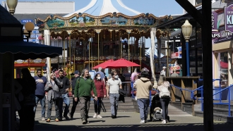 Masked and unmasked visitors walk in front of the carousel at Pier 39 in San Francisco