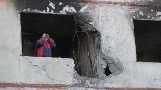 A man holds his head as he stands in his apartment in a multi-story house that was destroyed following a Russian attack
