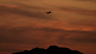 A passenger jet is silhouetted against the sky at dusk.
