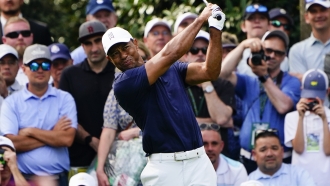 Tiger Woods swings a golf club with spectators behind him.