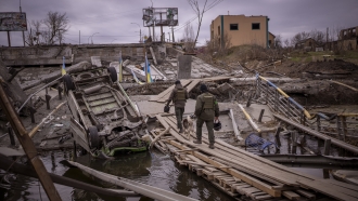 Ukrainian soldiers walk on a destroyed bridge