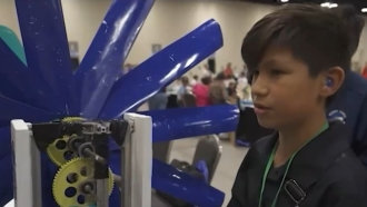 A student stands next to his wind turbine project during the KidWind Challenge