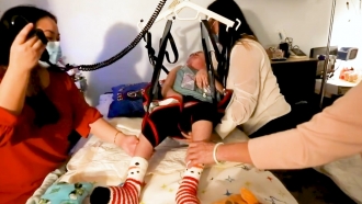 Child with condition lifted by medical swing above hospital bed