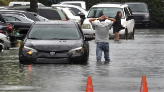 A driver climbs out of his stalled car after he tried to move it to higher ground from the flooded parking lot in Florida.