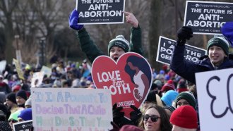 Anti-abortion protesters hold signs.