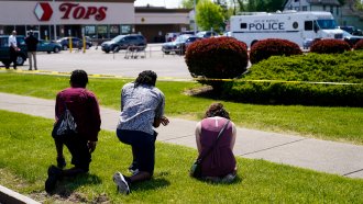 People kneel outside of Tops supermarket.