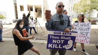 An anti-abortion activist holds his Bible and a message sign while abortion rights supporters hold counter signs and dance