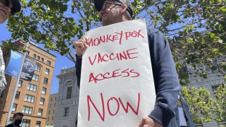 A man holds a sign advocating for monkeypox vaccine access