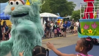 A performer dressed as the Sesame Street character Rosita waves off two young Black girls