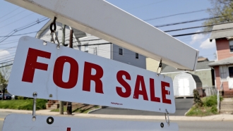 A "for sale" sign hangs from a post outside of a vacant business building