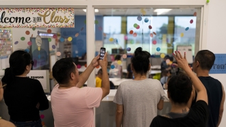 Parents of first-grade students watch their children through a classroom window on the first day back to school