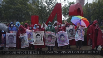 Friends and relatives seeking justice for the missing Ayotzinapa students gather round a monument dedicated to the student