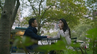 A man and woman sit down at a table in a park