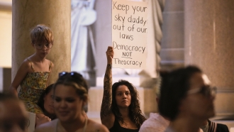 Demonstrators with signs stand outside the Indiana Statehouse in Indianapolis.