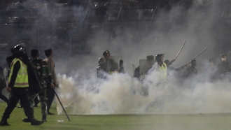 Police officers and soldiers stand amid tear gas smoke after clashes between fans during a soccer match at Kanjuruhan Stadium
