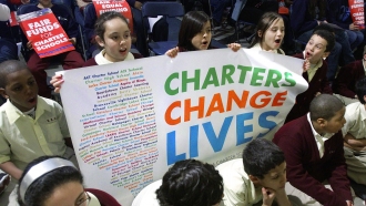 Students hold a sign saying, " Charters Change Lives."