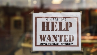 A help wanted sign is displayed in a storefront.