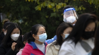 A worker wearing a face shield talks to people standing in line for COVID-19 tests.