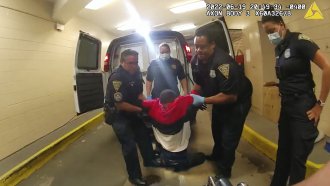 In an image from police body camera video, Richard "Randy" Cox, center, is pulled from the back of a police van.