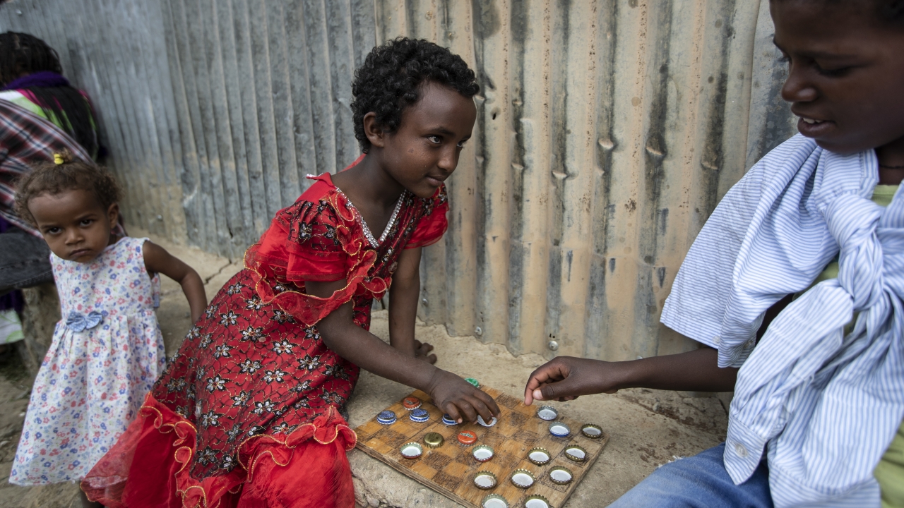 A little girl plays a game of checkers using soda bottle tops with friend at a center for center for displaced Tigrayans.