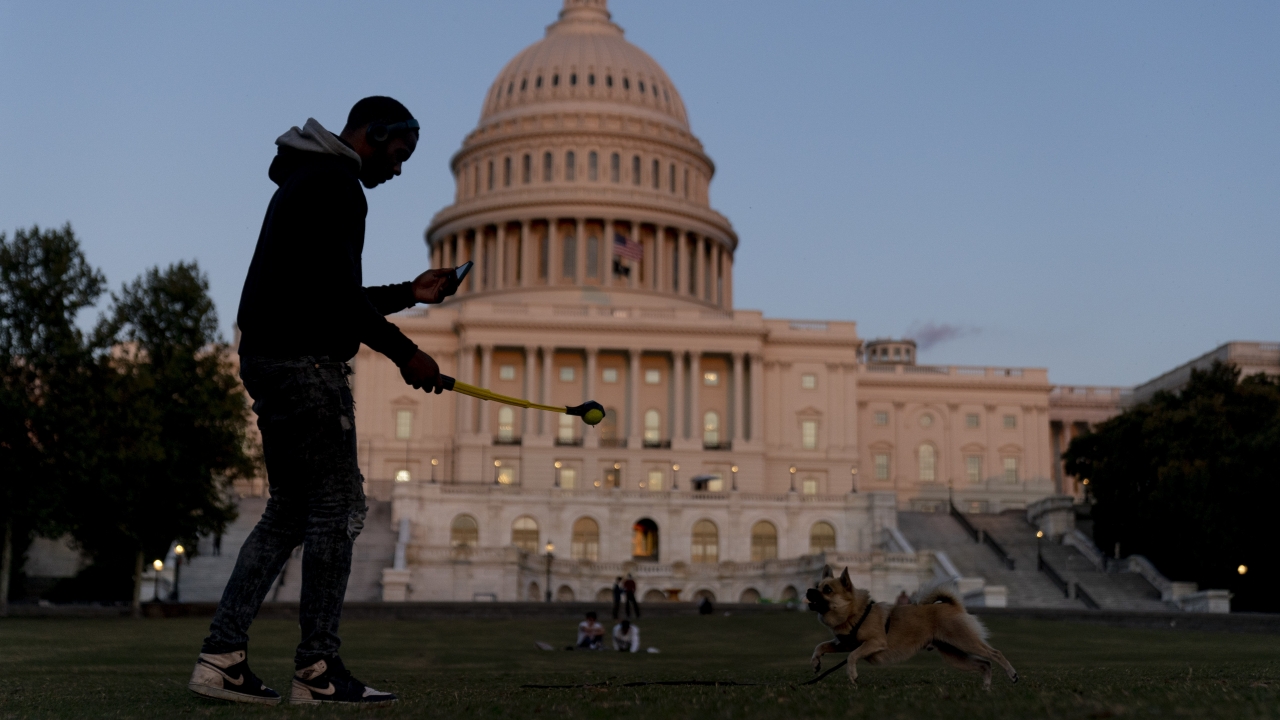 The U.S Capitol is visible at sunset as a man plays fetch with a dog in Washington, D.C.