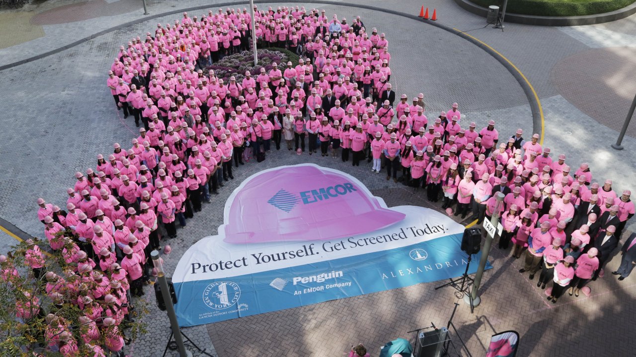 Hundreds of New Yorkers wearing pink hard hats and pink shirts form a pink ribbon in honor of Breast Cancer Awareness Month