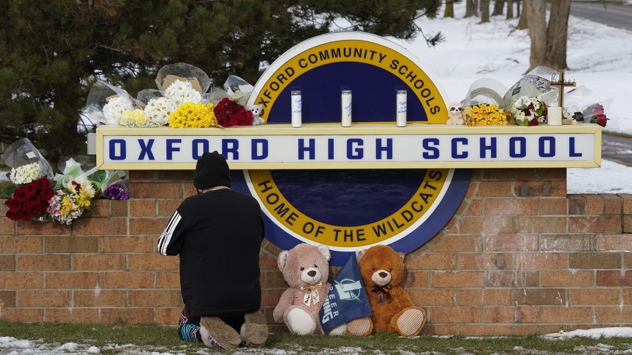 A well wisher kneels to pray at a memorial on the sign of Oxford High School