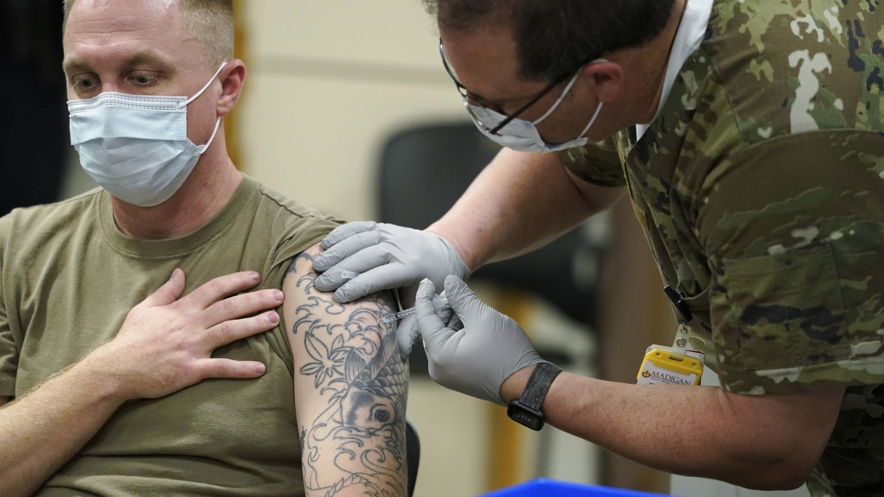 Staff Sgt. Travis Snyder, left, receives the first dose of the Pfizer COVID-19 vaccine given at Madigan Army Medical Center